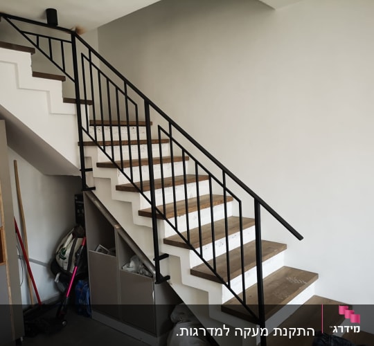 מעקה מתכת שחור על מדרגות עץ ולבן